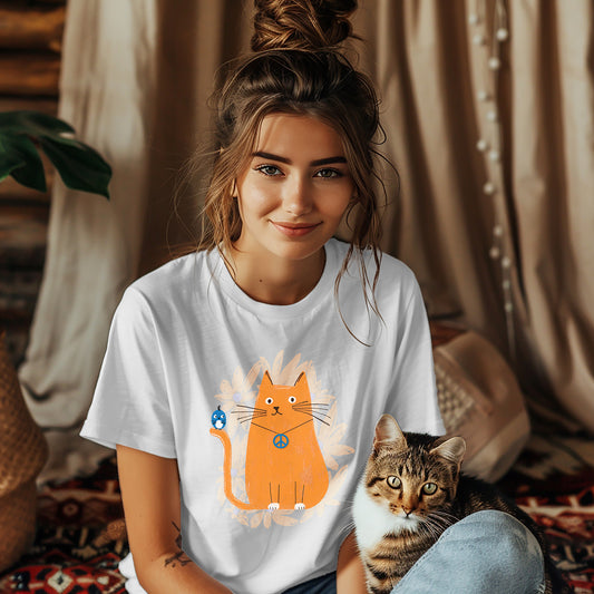 Woman wearing a white t-shirt featuring on the front an orange cat wearing a "peace" sign necklace; perched on the cat's tail is a cute blue bird. A spray of pale orange flowers in the background.