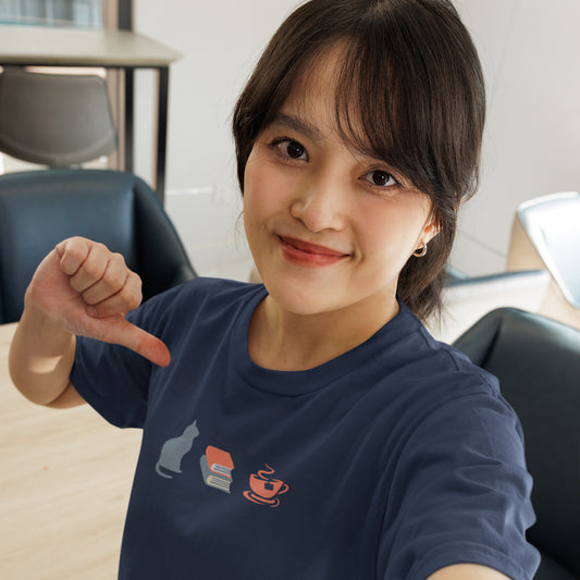 Woman wearing a navy blue graphic tee showing a powder-blue cat, orange and blue books, and orange tea cup.