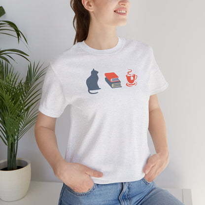 smiling woman wearing a light gray heather graphic tee showing a powder-blue cat, orange and blue books, and orange tea cup