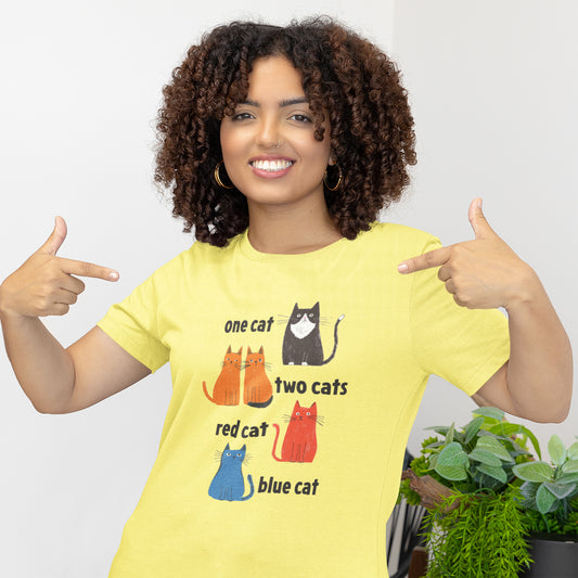 woman wearing a bright yellow graphic t-shirt featuring one tuxedo cat, two orange cats, one red cat, and one blue cat